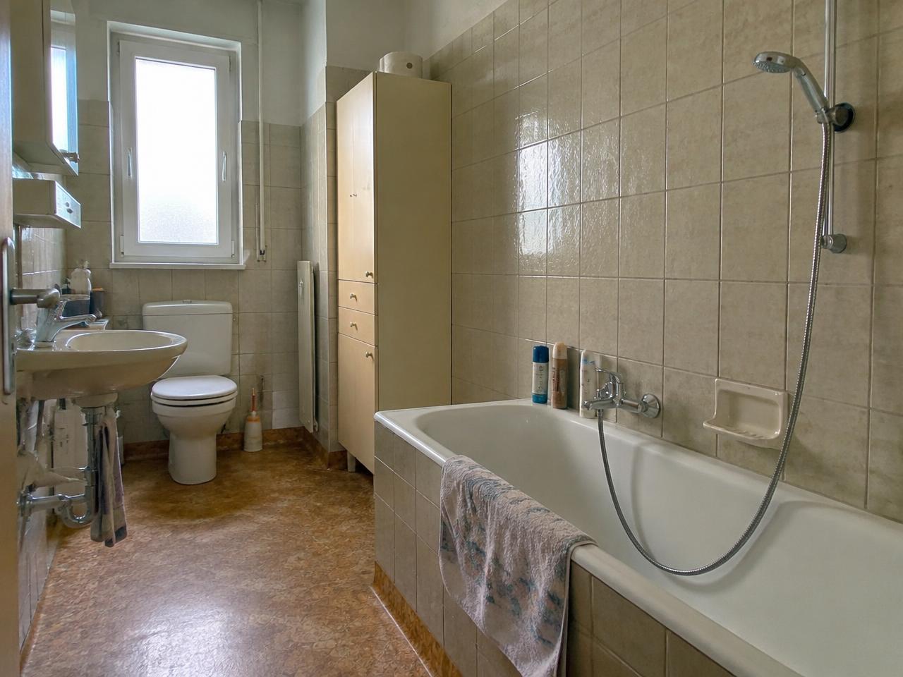 Älteres Badezimmer in einer Zürcher Wohnung mit beigen Fliesen und Badewanne vor der Sanierung